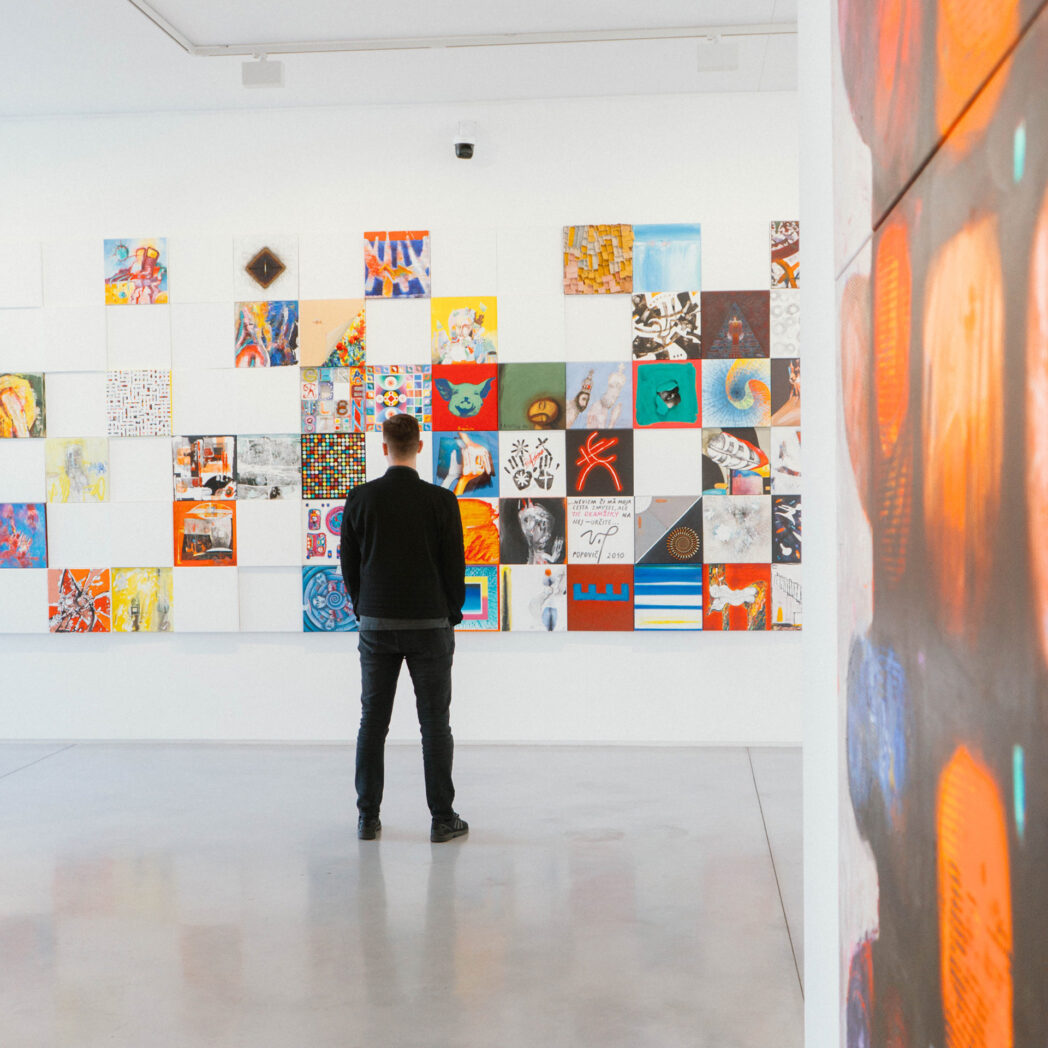 a man looking at a gallery wall full of colorful art