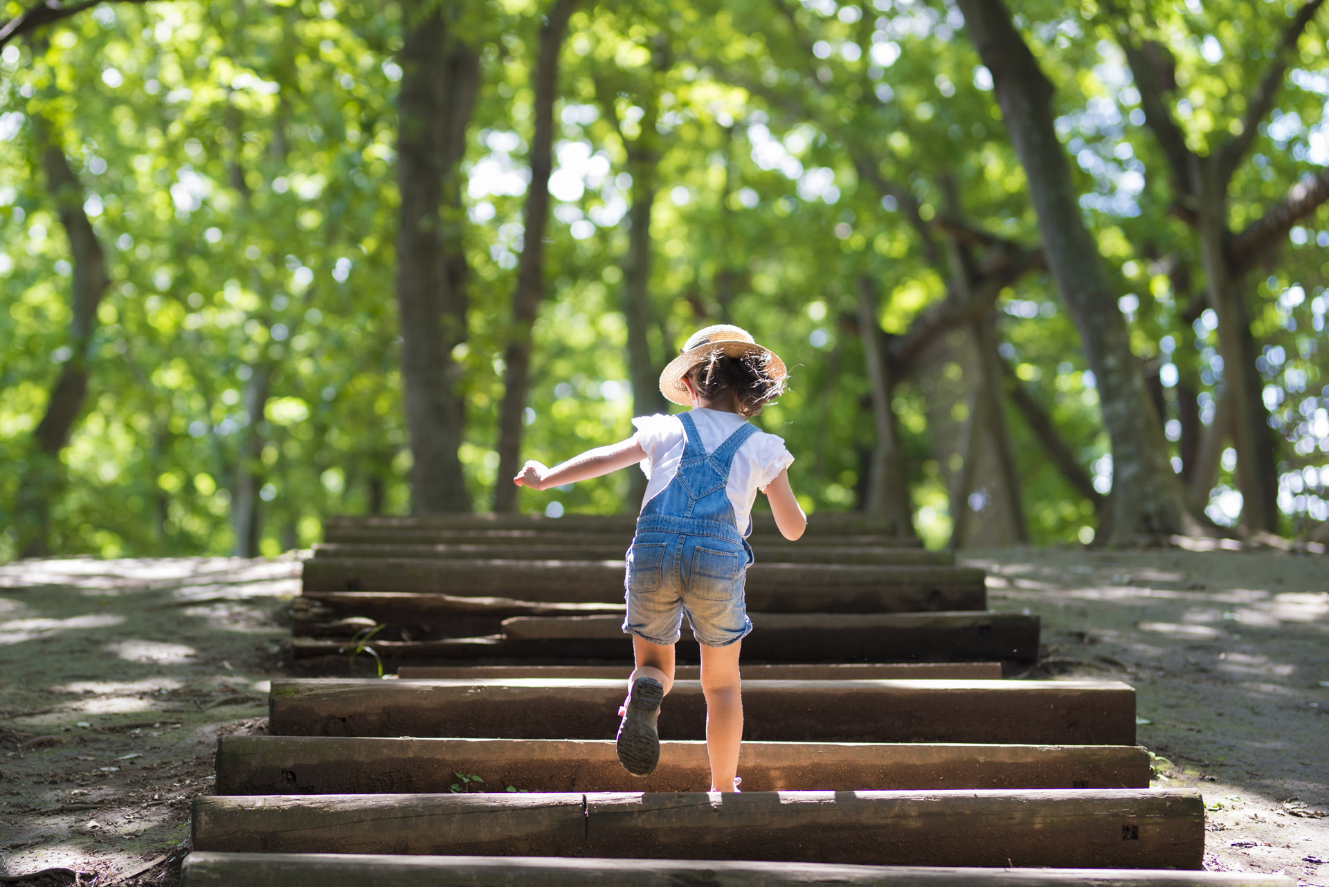 small girl in overalls climbing a forest staircase